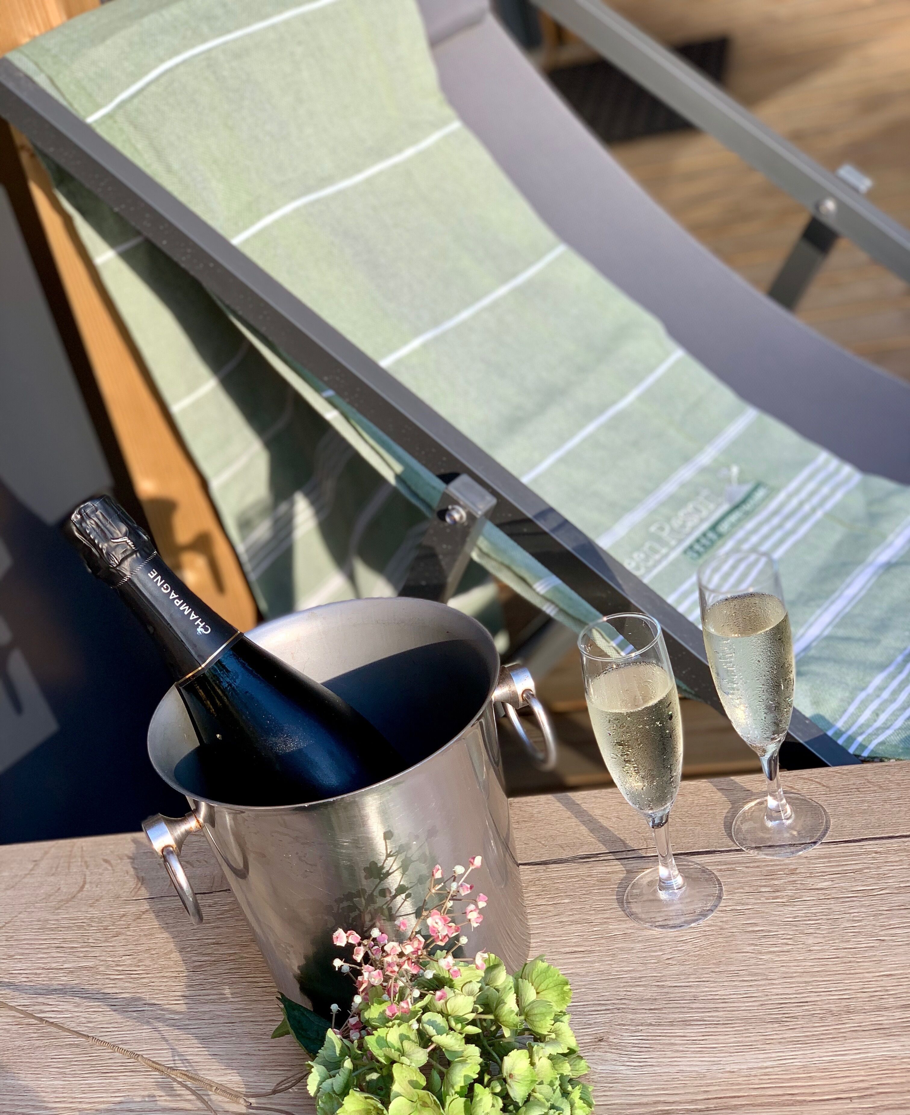 Ein Metallkübel mit einer Flasche, zwei Sektgläsern und einer kleinen Pflanze auf einem Holztisch.