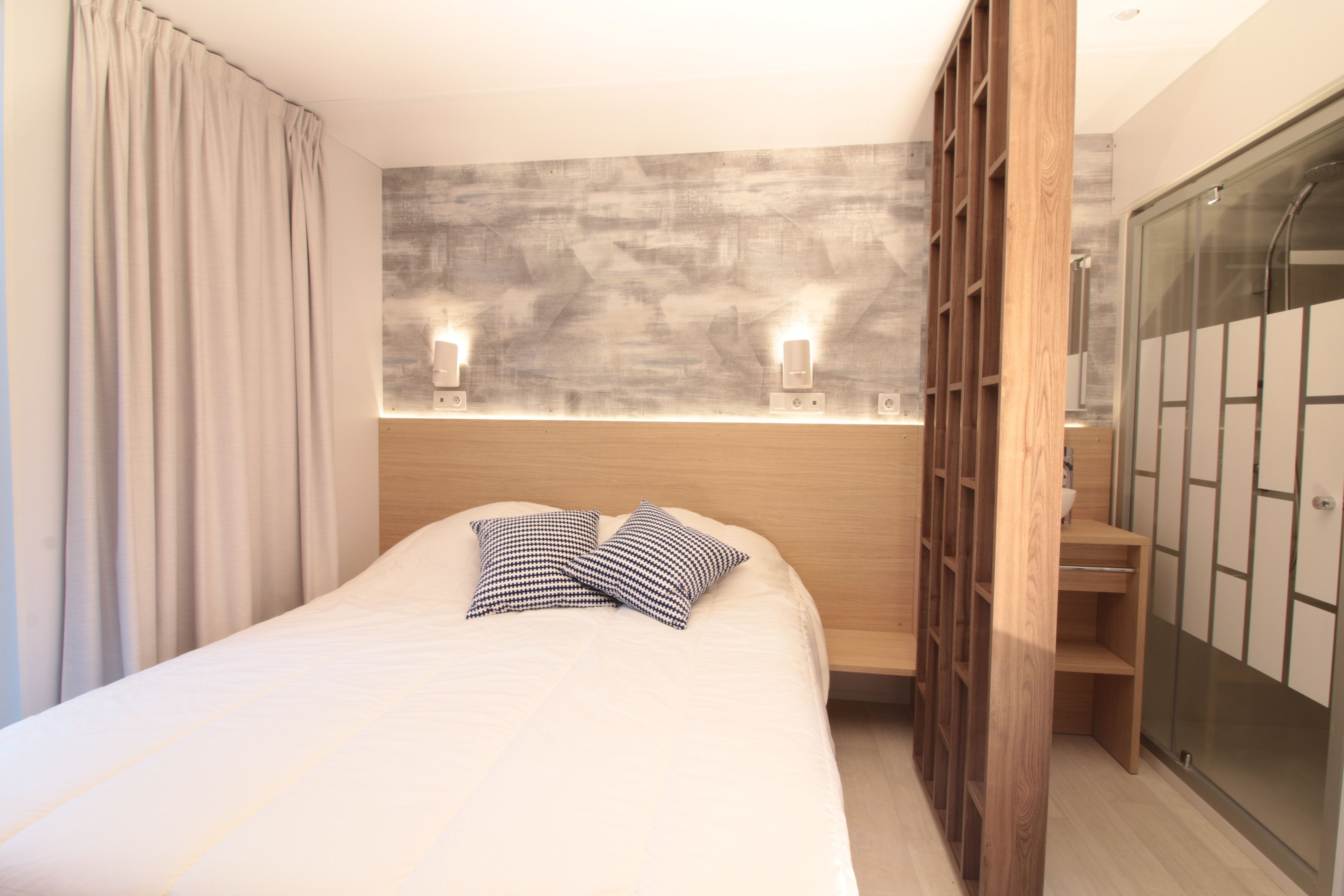 A modern bedroom with a large bed, two bedside lamps, a wooden wardrobe, and a glass shower enclosure.