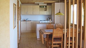 Una cocina compacta con armarios de madera, una mesa de comedor con sillas y una ventana con cortina.