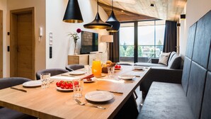 Un espace repas avec une longue table, des chaises et un banc. On y trouve des assiettes, des verres et des couverts.