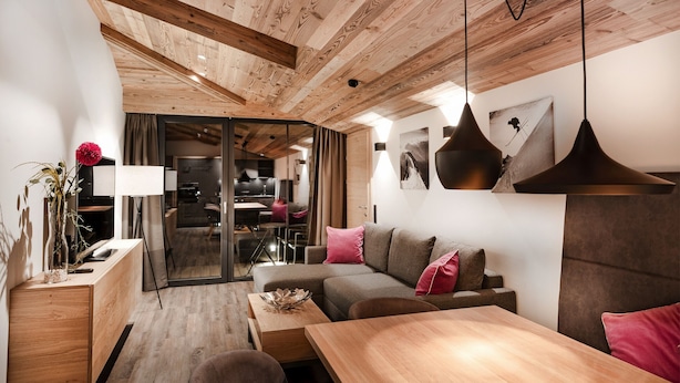 Un salon moderne avec un plafond en bois, un canapé, une table à manger et une porte en verre donnant sur la cuisine.