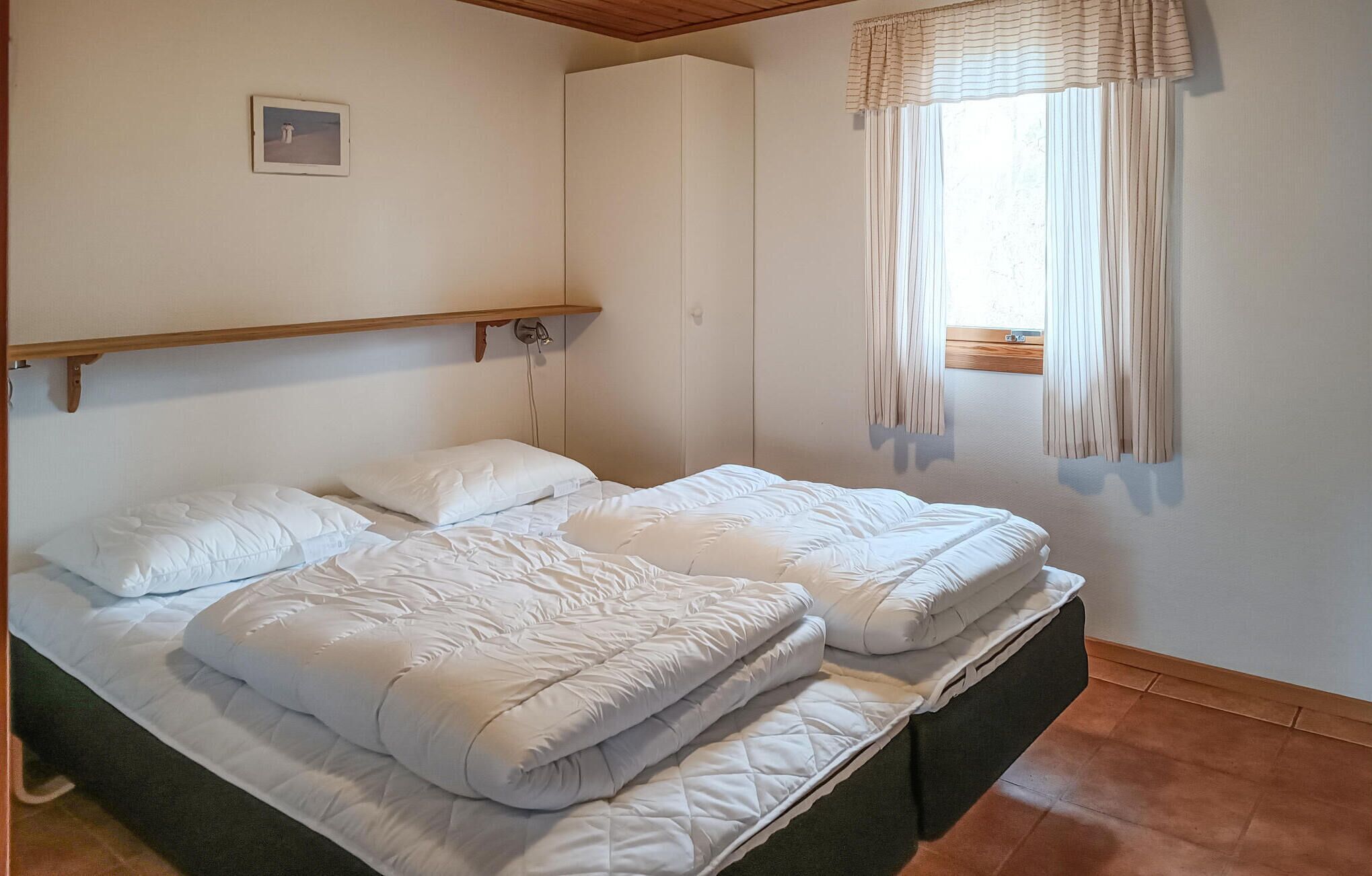 A double bed with white bedding in a room with a wooden ceiling and a window with curtains.