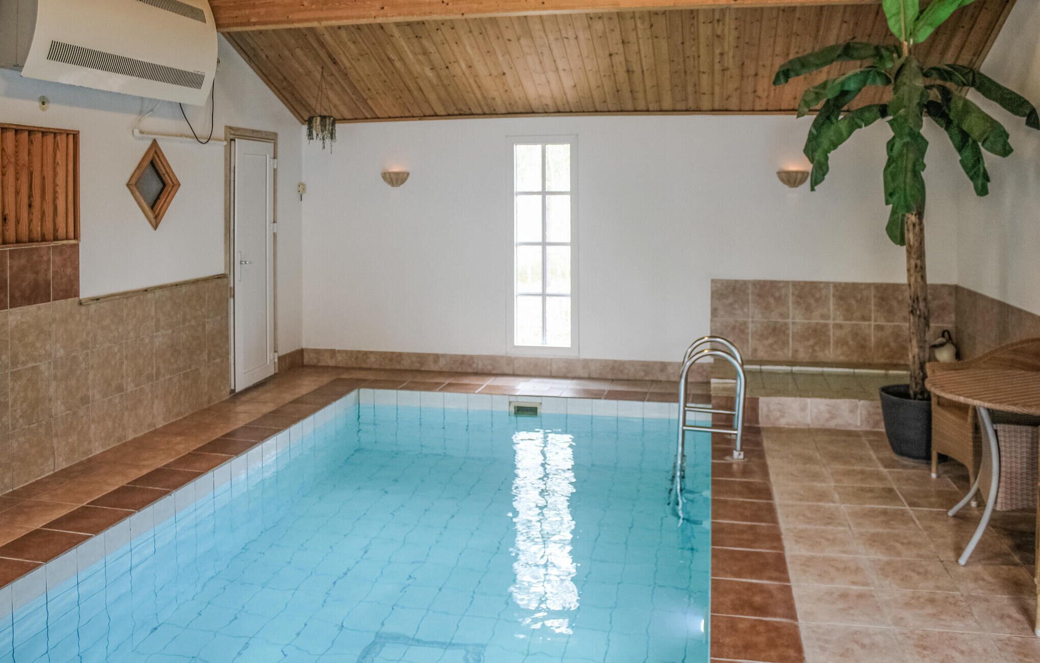 Uma piscina com escada, teto de madeira, janela e planta em vaso.