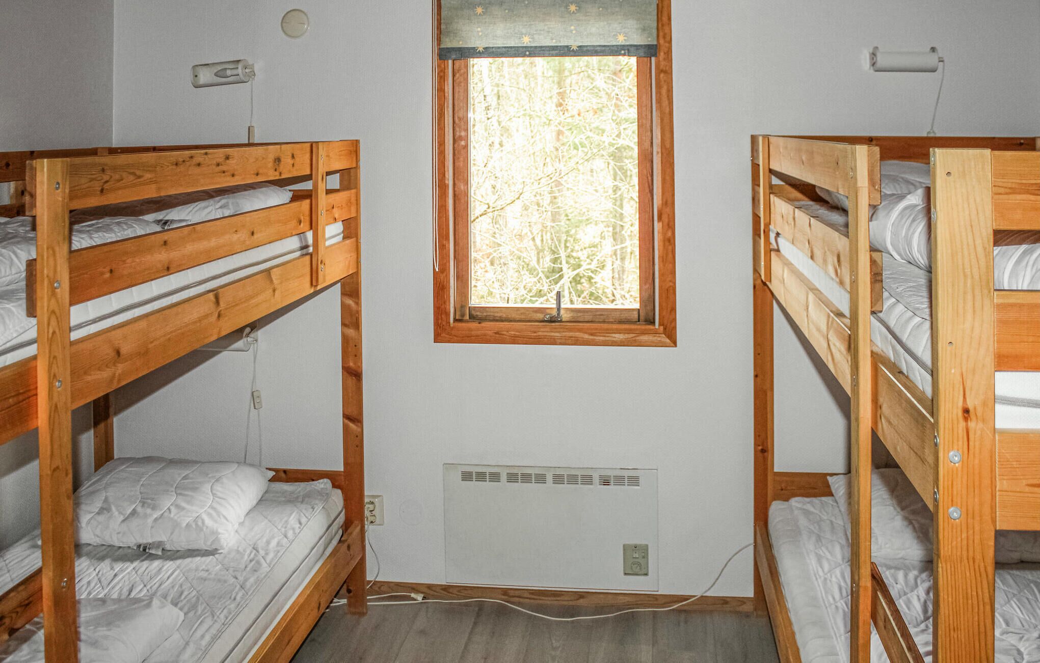A dormitory room with two bunk beds, a window with a view of trees, and a wall-mounted heater.