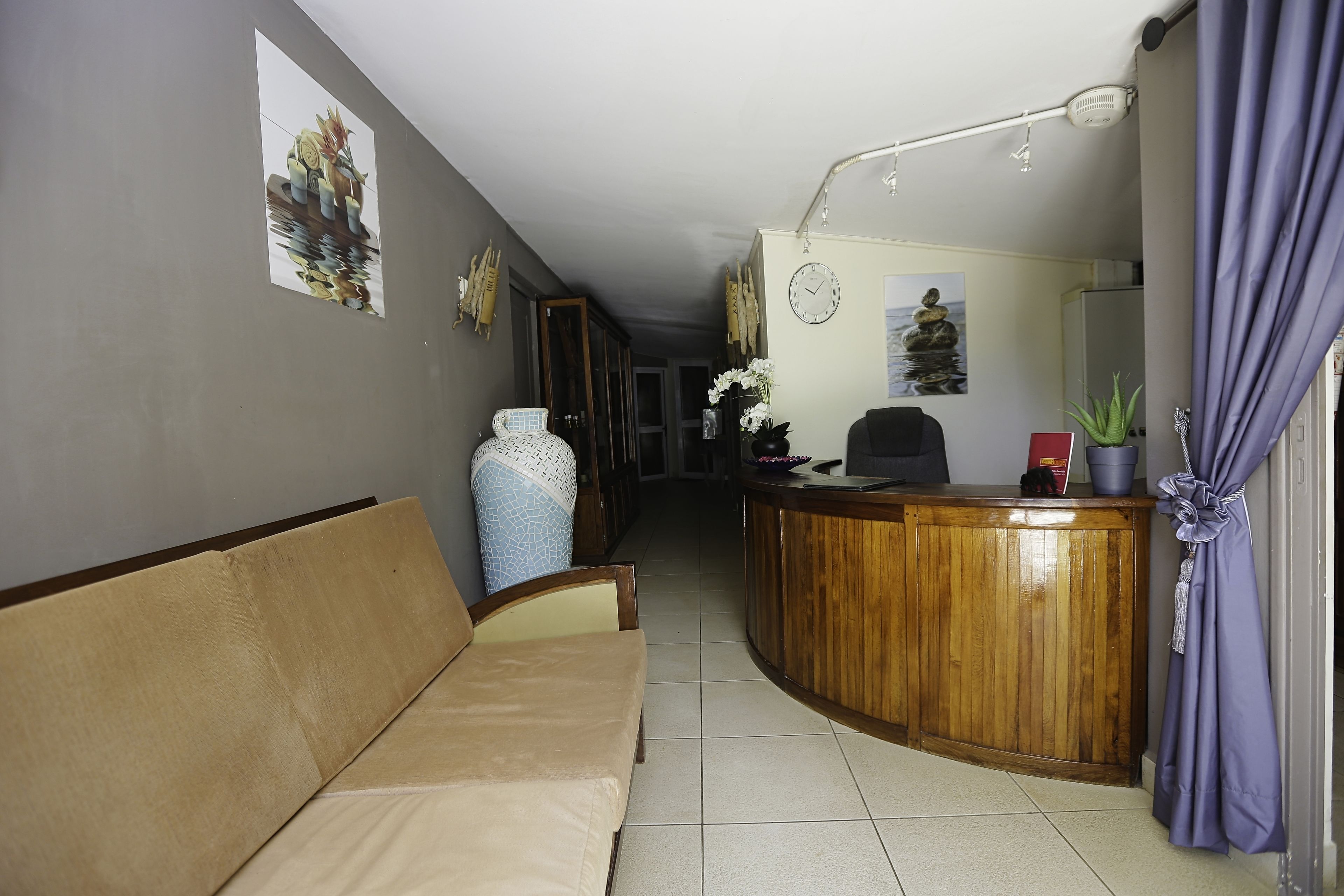Un espace d’accueil avec un comptoir de réception en bois, un canapé et une horloge au mur.