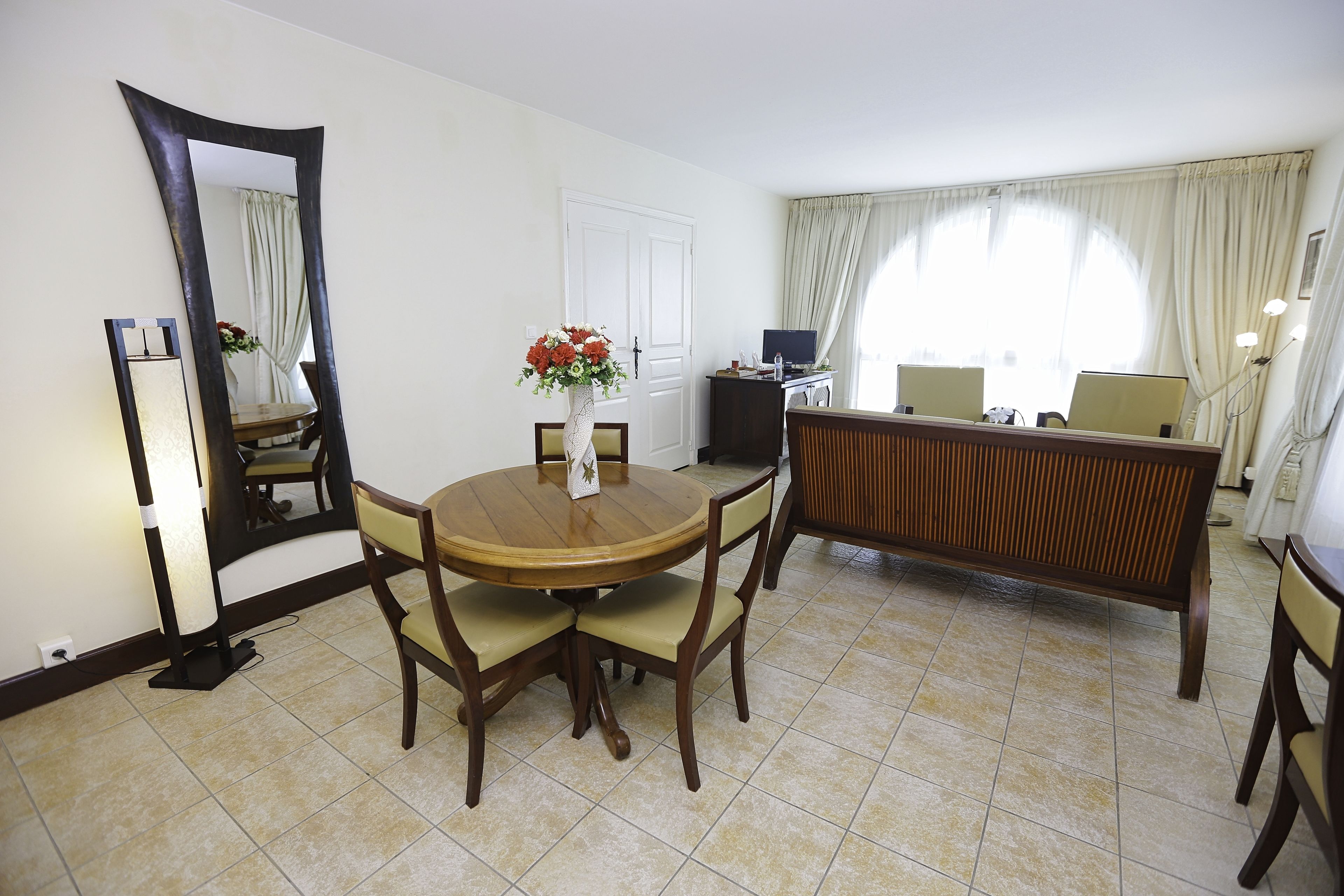 Habitación de hotel con una mesa de comedor redonda, sillas, un televisor y un espejo grande.