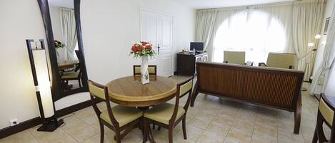 Habitación de hotel con una mesa de comedor redonda, sillas, un televisor y un espejo grande.
