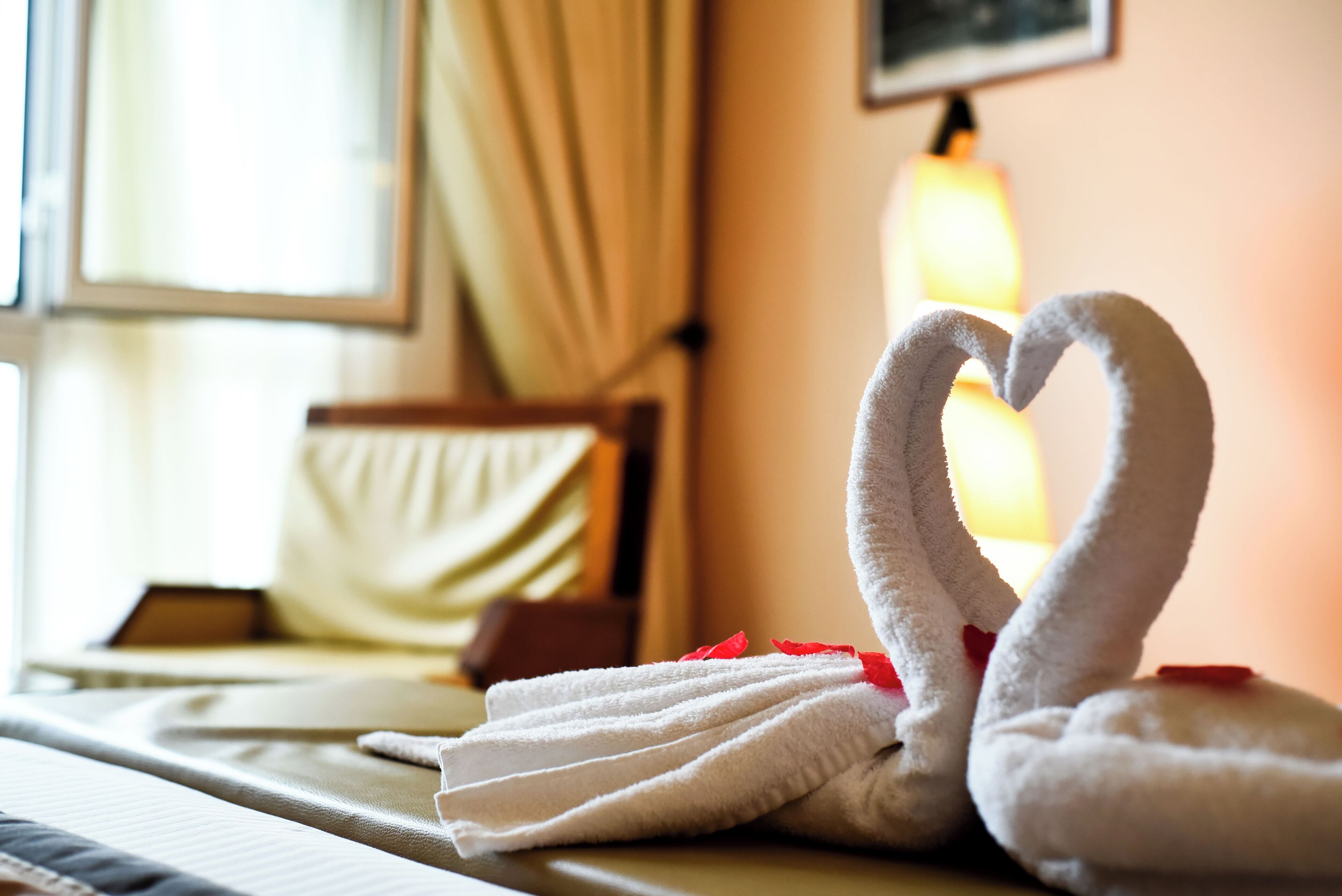 A neatly made swan-shaped towel arrangement on a hotel bed with a lamp in the background.