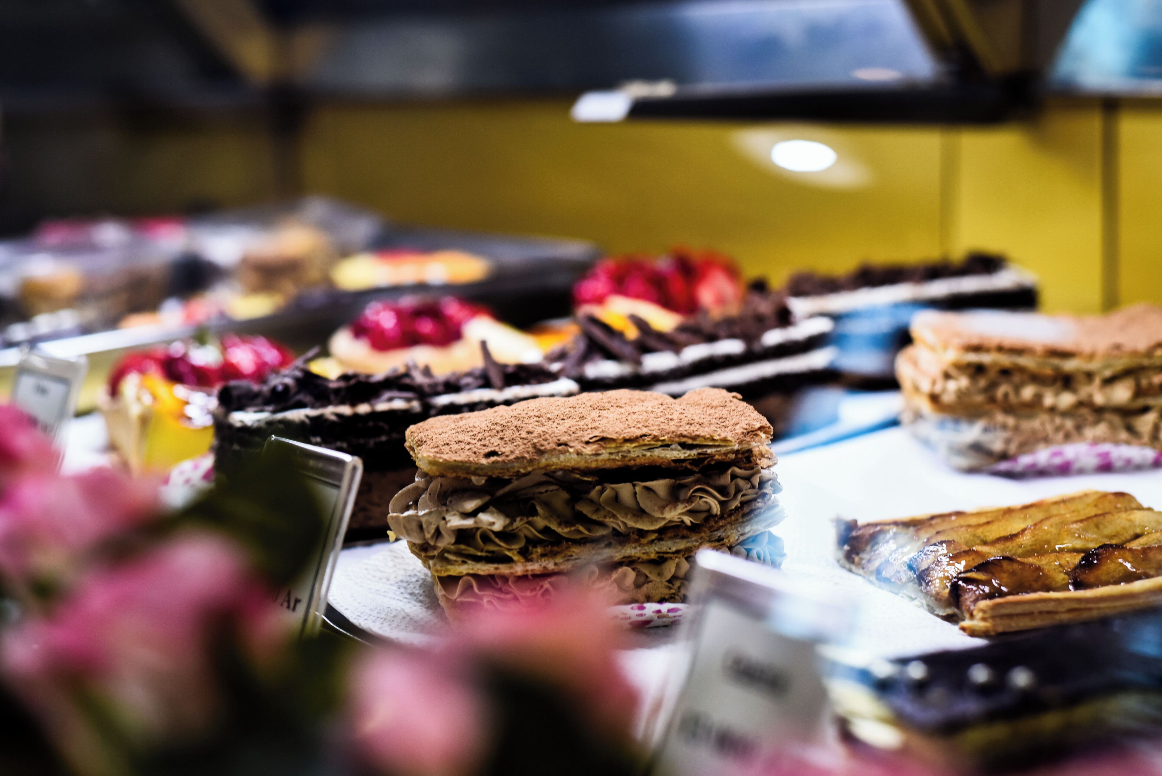 A display of various desserts, including layered cakes and pastries, in a bakery setting.