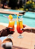 Dos personas sosteniendo altos vasos de una bebida colorida con pajitas y rodajas de limón, junto a una piscina.