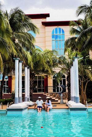 Un área de piscina con palmeras, un edificio con ventanas de arco y una estatua de toro.