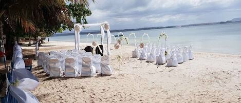 Decoración para una boda en la playa, con sillas blancas y un toldo.