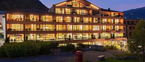 Un hotel de varios pisos con balcones, un patio interior y el paisaje de una montaña al fondo.