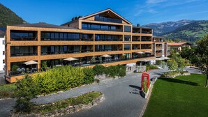 Un hotel de varios pisos con terraza exterior, una cabina telefónica roja y montañas al fondo.