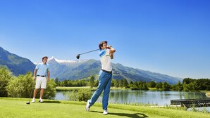 Un campo de golf con un lago y montañas al fondo.