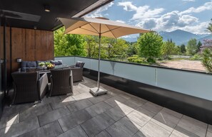 A balcony with a dining set, a large umbrella, and a view of mountains.