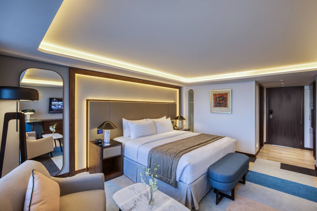 A modern hotel room with a large bed, bedside tables, a desk, and a seating area.
