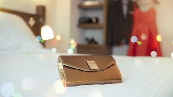 Uma clutch marrom bem dobrada sobre uma cama, com um fundo desfocado mostrando um vestido vermelho e prateleiras.