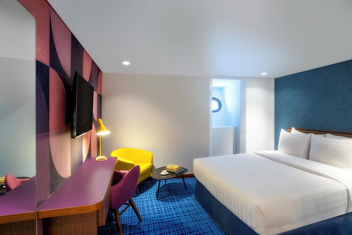 A hotel room with a bed, a desk, a chair, and a TV on the wall.