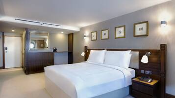 Quarto de hotel com uma cama grande, mesas de cabeceira, um espelho e quadros nas paredes.