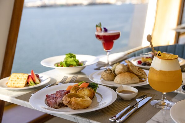 A dining table with various dishes, including a salad, bread, and meat, and a drink with a lemon garnish.