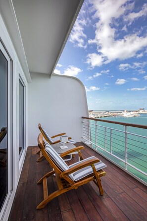 A balcony with wooden chairs and a table, overlooking a marina and the sea.