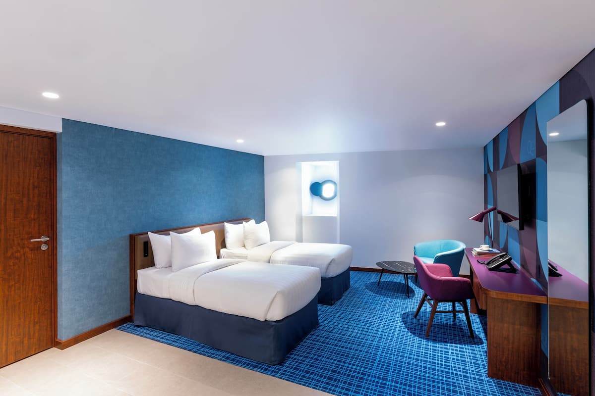 A modern hotel room with a large bed, a desk, a chair, and a small table.