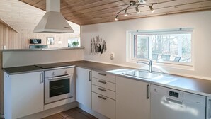 Una cocina moderna con armarios blancos, horno integrado, lavavajillas y una ventana que proporciona luz natural.