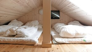 Un dormitorio abuhardillado pequeño con dos camas, paredes de madera y un tragaluz.