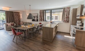 Cozinha moderna com área de jantar, piso de madeira e uma grande janela com cortinas.