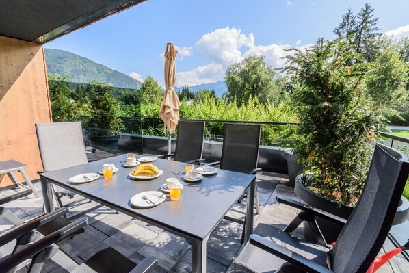 An outdoor dining area with a table set for two, chairs, and a potted plant.