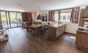 A modern kitchen with a dining area, wooden flooring, and large windows.