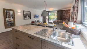 A modern kitchen with a central island, a dining area with a table and chairs, and a large window with curtains. - SR, Top 3 - Ap. 100m² mit 3 SZ, Terrasse 24m² (Zell am See)