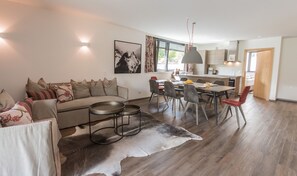 Uma sala de estar moderna com sofá, mesa de jantar e cadeiras, área de cozinha e uma janela grande.