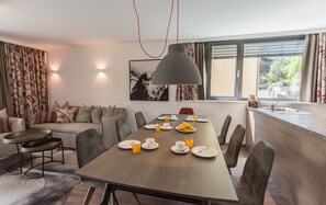 Uma sala de jantar moderna com uma mesa de madeira posta para o café da manhã, um sofá e uma janela grande com persianas.