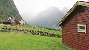 Een landelijk landschap met een rode houten constructie, een schuur en een stenen muur.