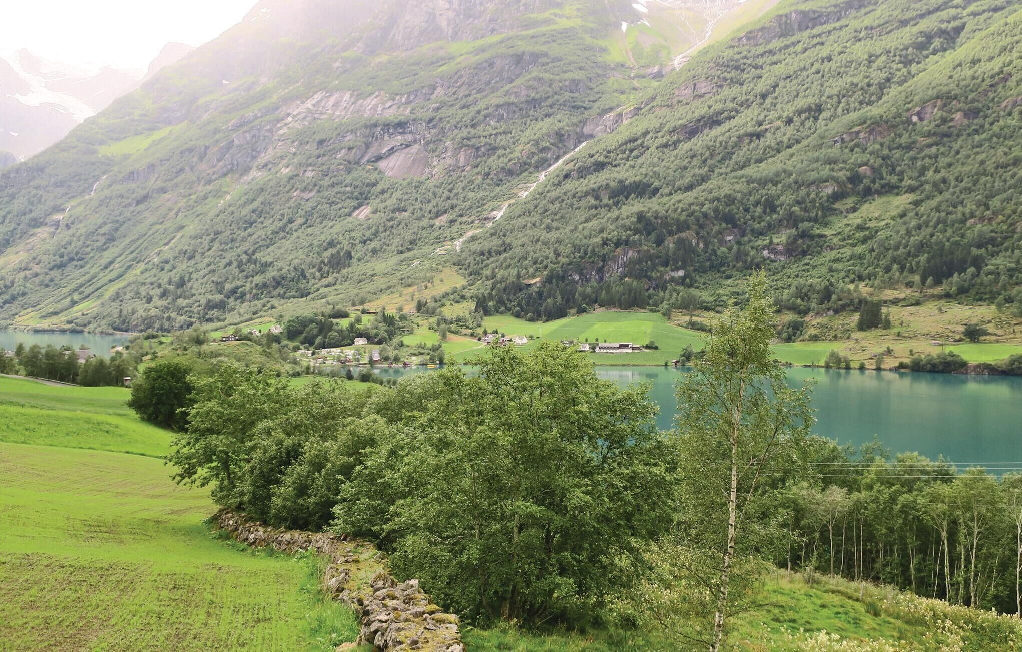 Een bergachtig landschap met een meer, groene velden en verspreide gebouwen.