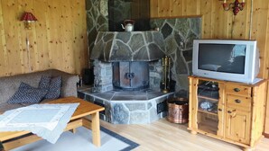 Een gezellige woonkamer met een stenen openhaard, houten meubels en een televisie op een houten kast.