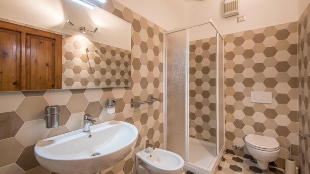 Ein Badezimmer mit sechseckischem Fliesendesign, einem Waschbecken, einem Bidet, einer Toilette und einer Duschkabine.