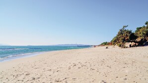 Ein weiter Sandstrand mit Fußspuren, einem klaren blauen Himmel und einer entfernten Brücke.