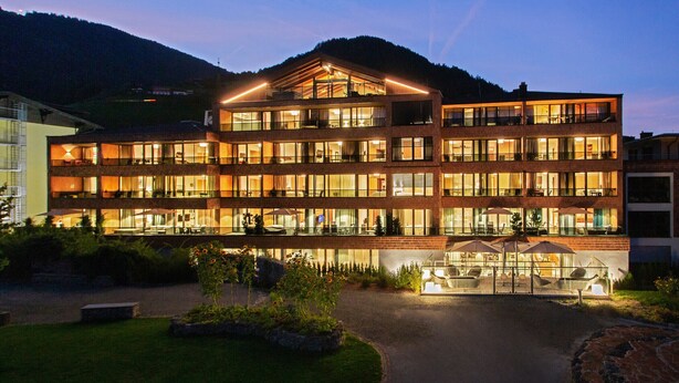 A multi-story hotel with a prominent entrance, outdoor seating, and a mountainous backdrop. - SR, Top 8 - Ap. 100m² mit 3 SZ, Terrasse 11 m² (Zell am See)