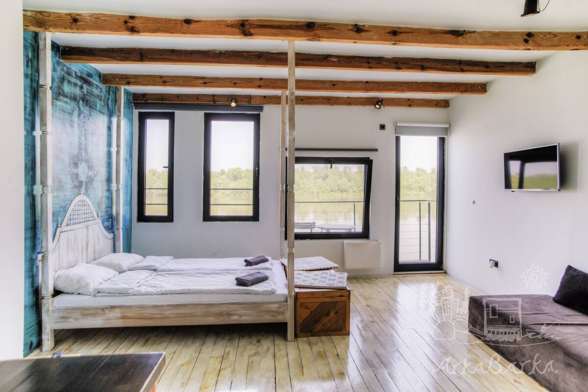 A bedroom with a wooden bed, a TV, and large windows.