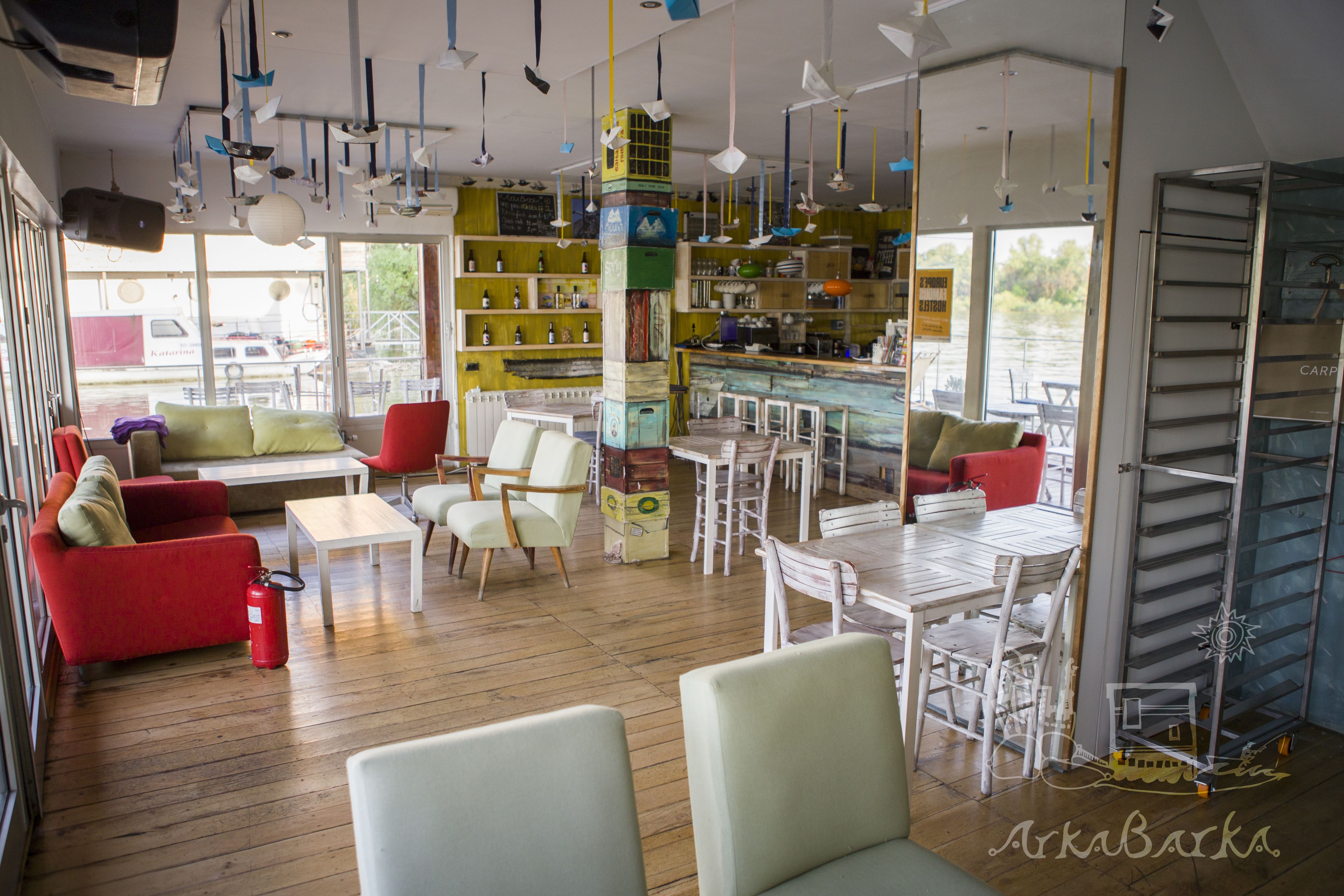 A cozy interior with a wooden floor, red and white furniture, and a bar area with shelves of bottles.