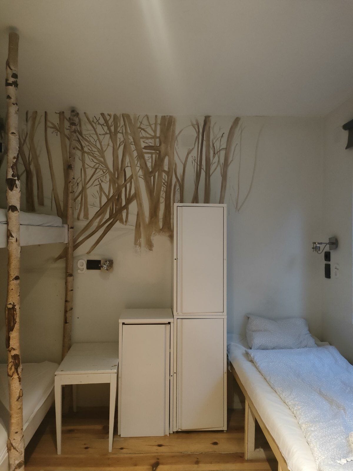 Una habitación pequeña y funcional con una cama litera, una mesita y un refrigerador.