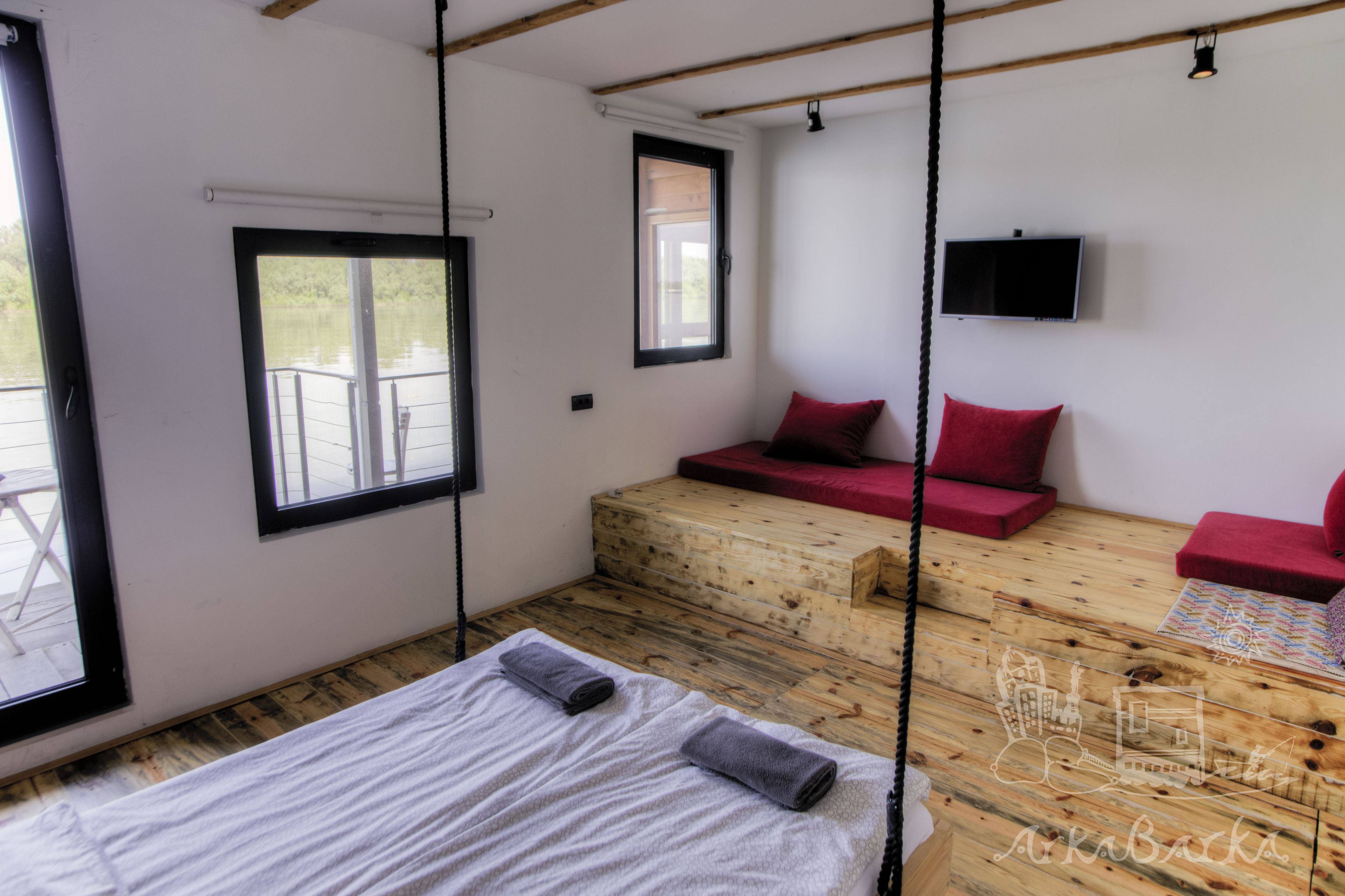 Een kamer met een bed, een houten bankje en een aan de muur bevestigde televisie.