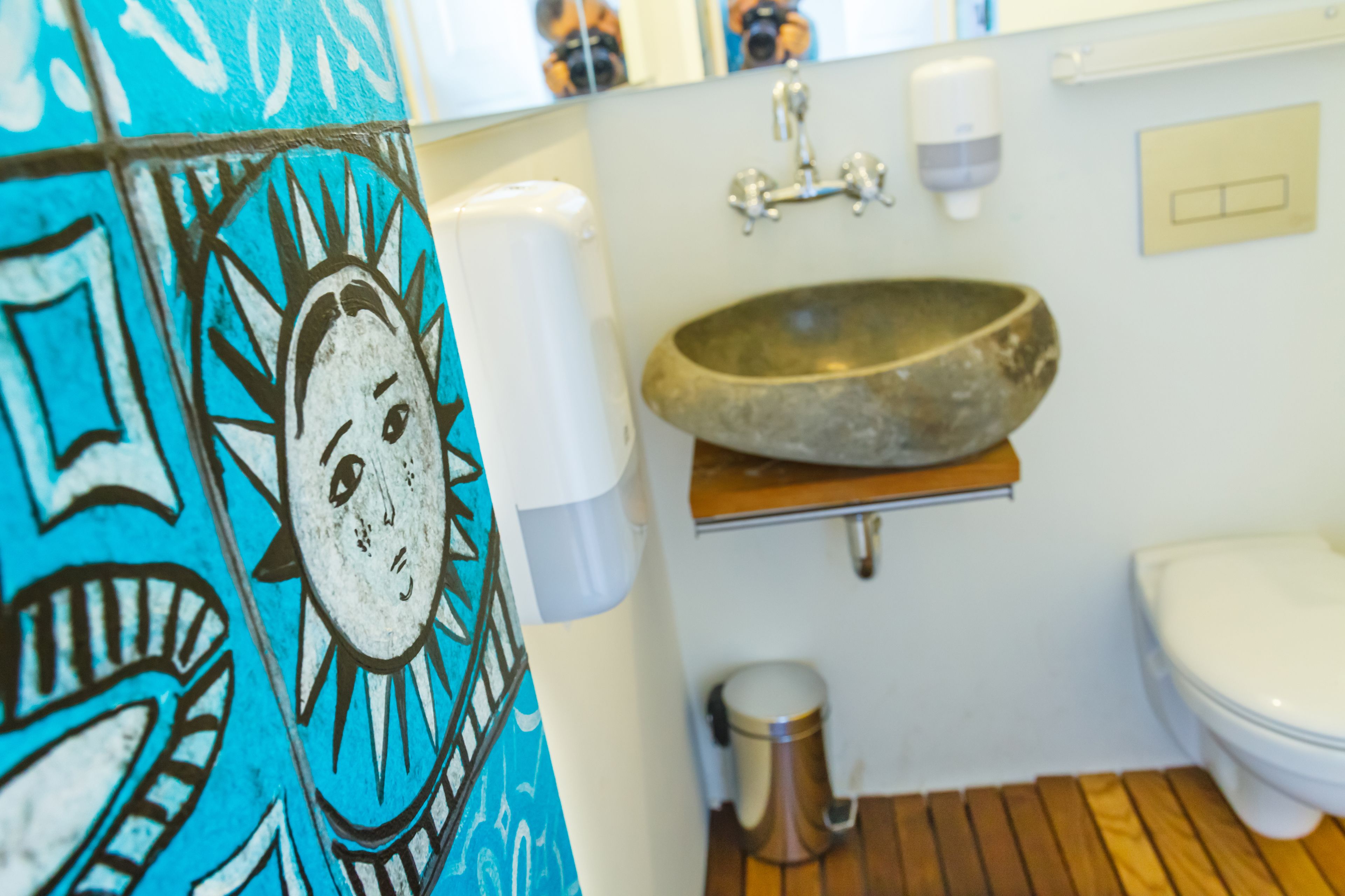 A bathroom with a stone sink, a toilet, a hand soap dispenser, and a trash can.