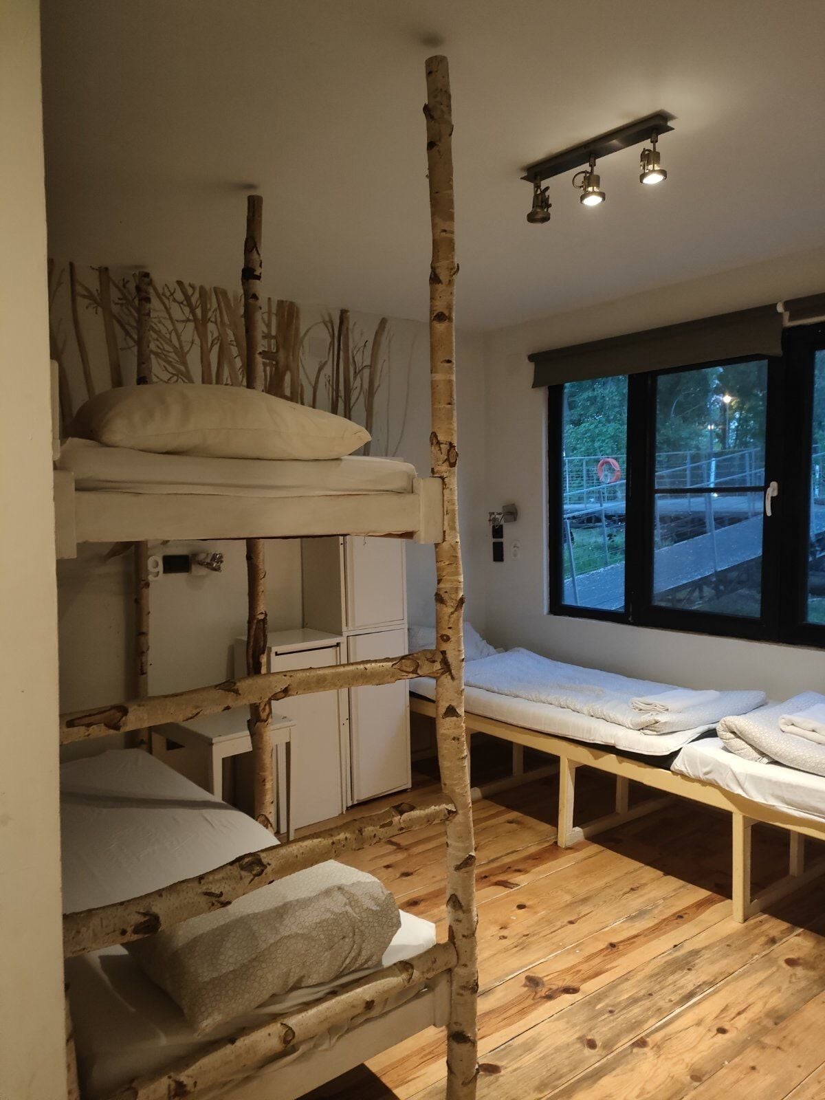 A bunk bed room with a wooden ladder, a desk, and a window with a view of the outside.