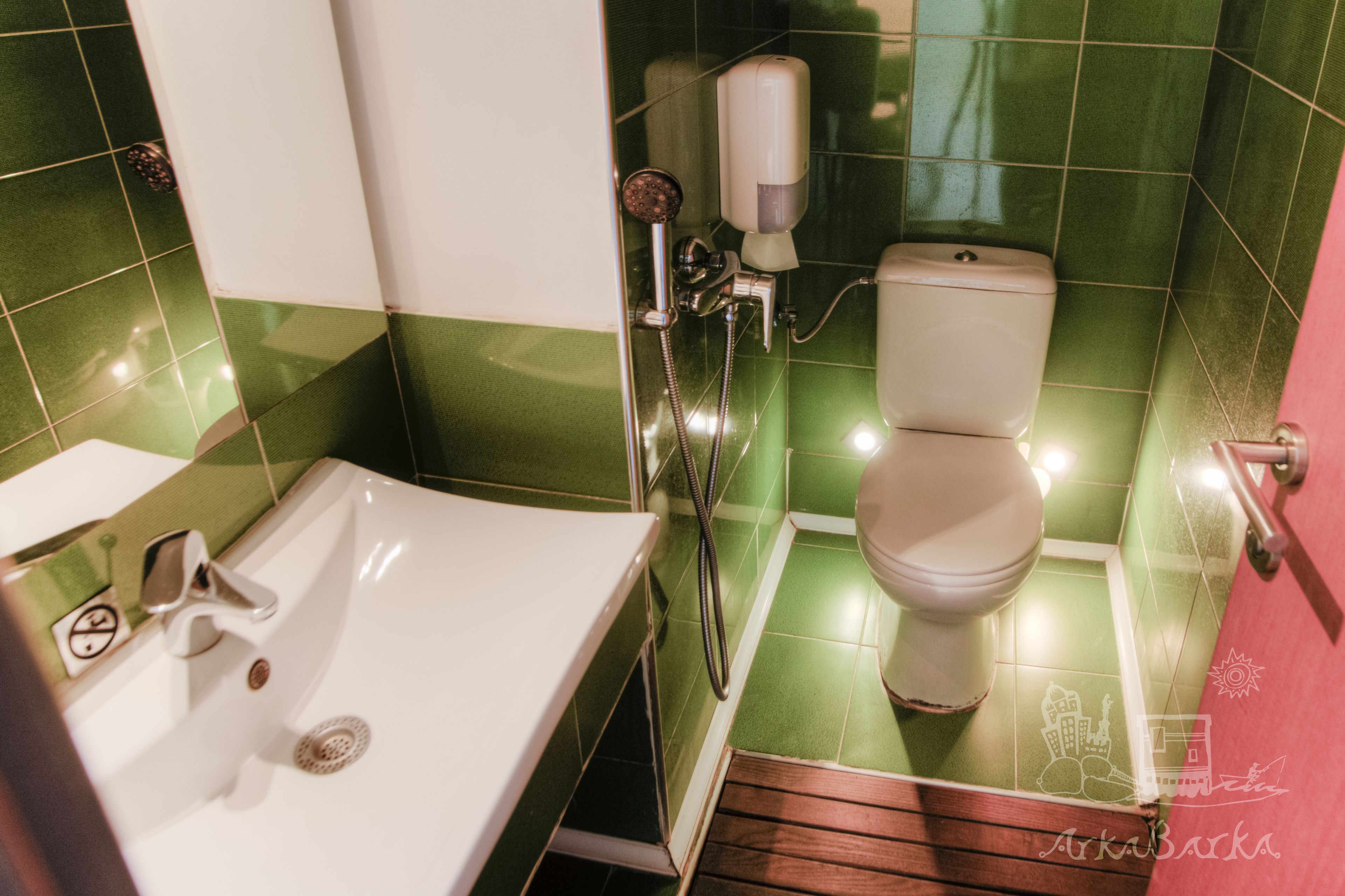 A bathroom with a white sink, green tiles, a toilet, and a shower head.