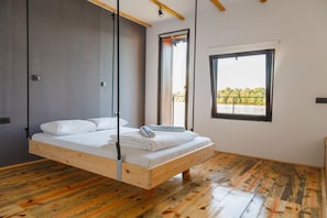 Habitación con cama de madera suspendida del techo, un ventanal con vistas a árboles y suelo de madera.
