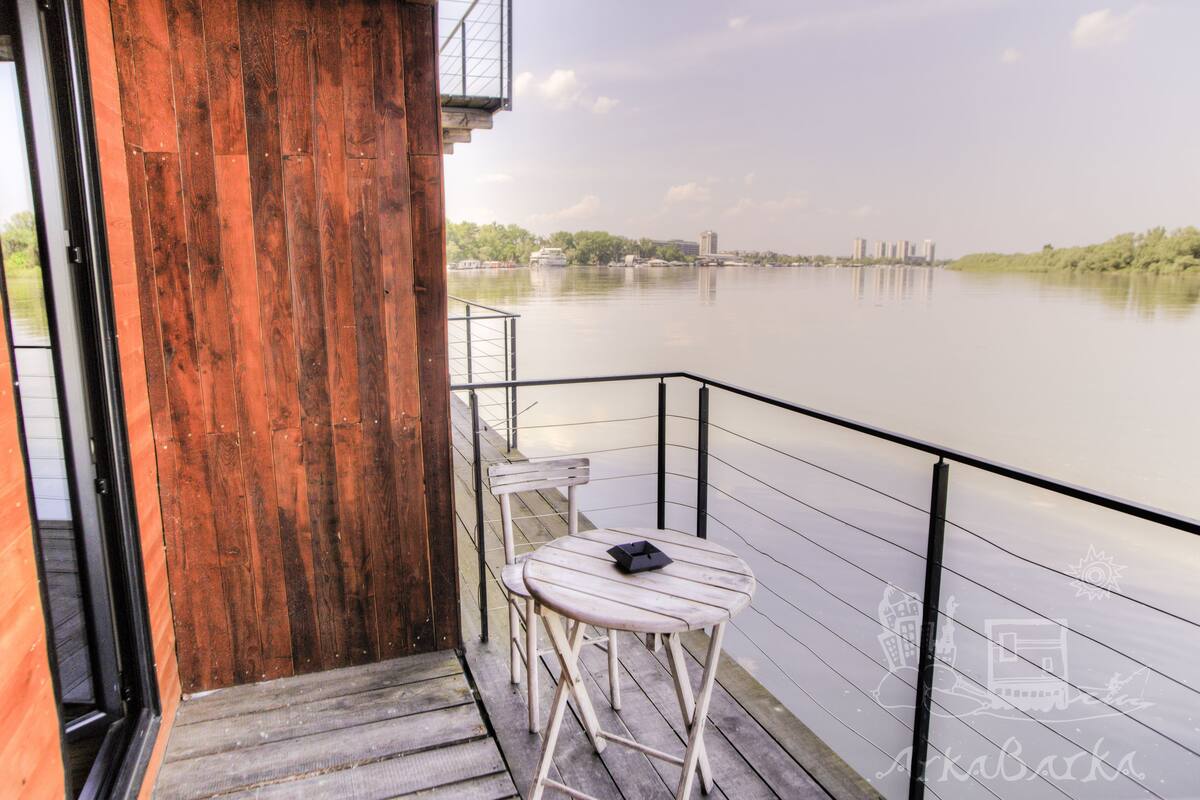 A wooden balcony with a table and chairs overlooking a calm river.